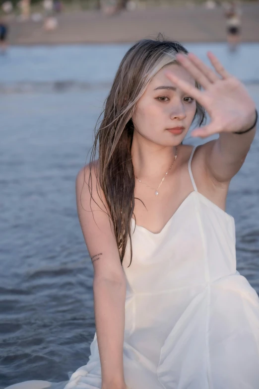 woman in white dress sitting on rocks at the edge of the water