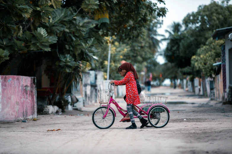 a young woman wearing a red polka dot outfit hes a pink bicycle along an urban street