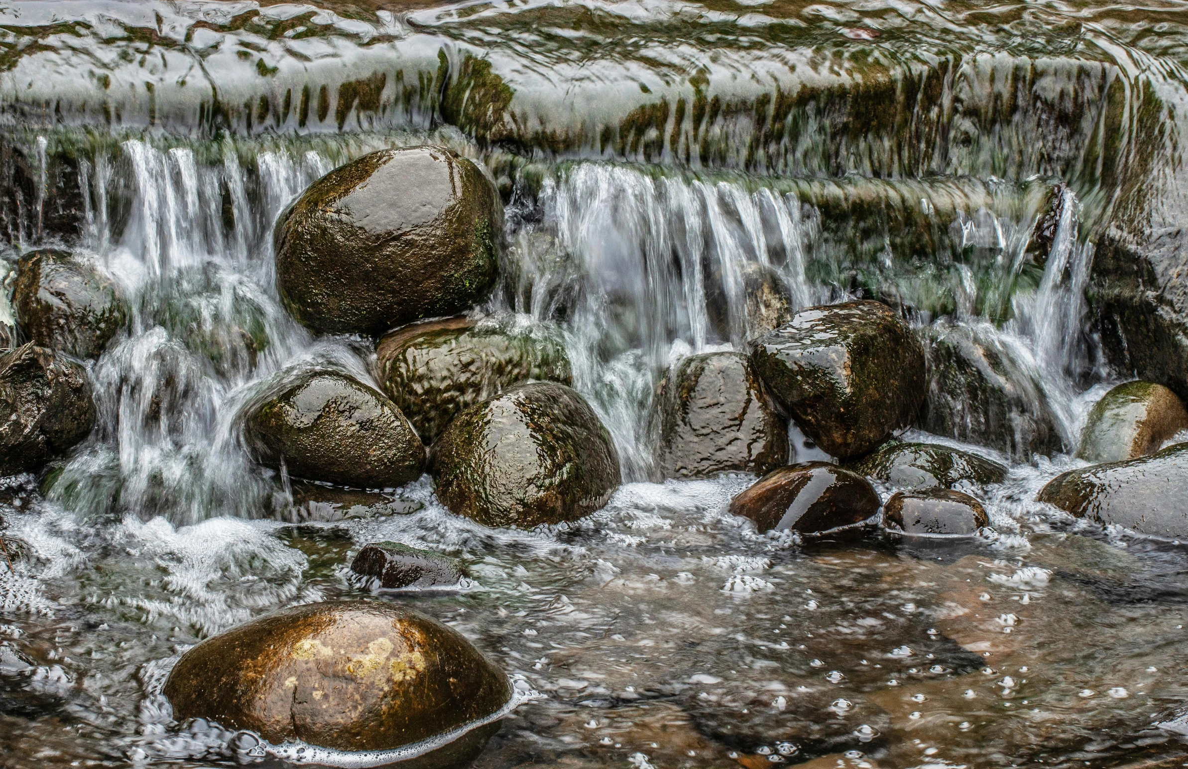 the flowing river is very colorful with rocks and moss