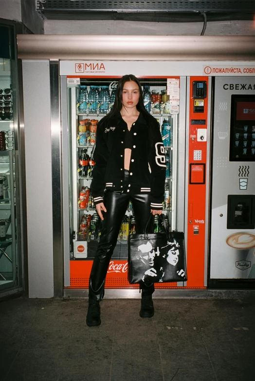 a woman in leather clothes stands next to a vending machine