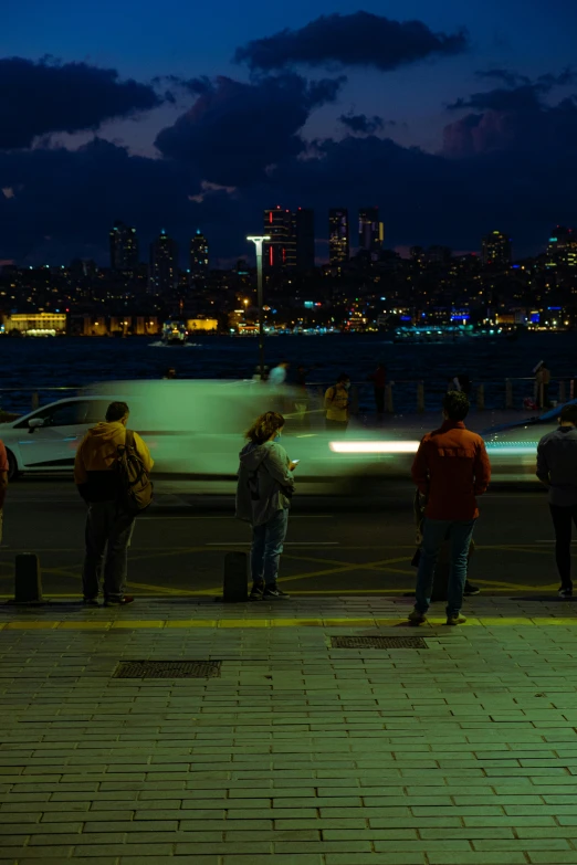 several people standing on the curb next to boats at night