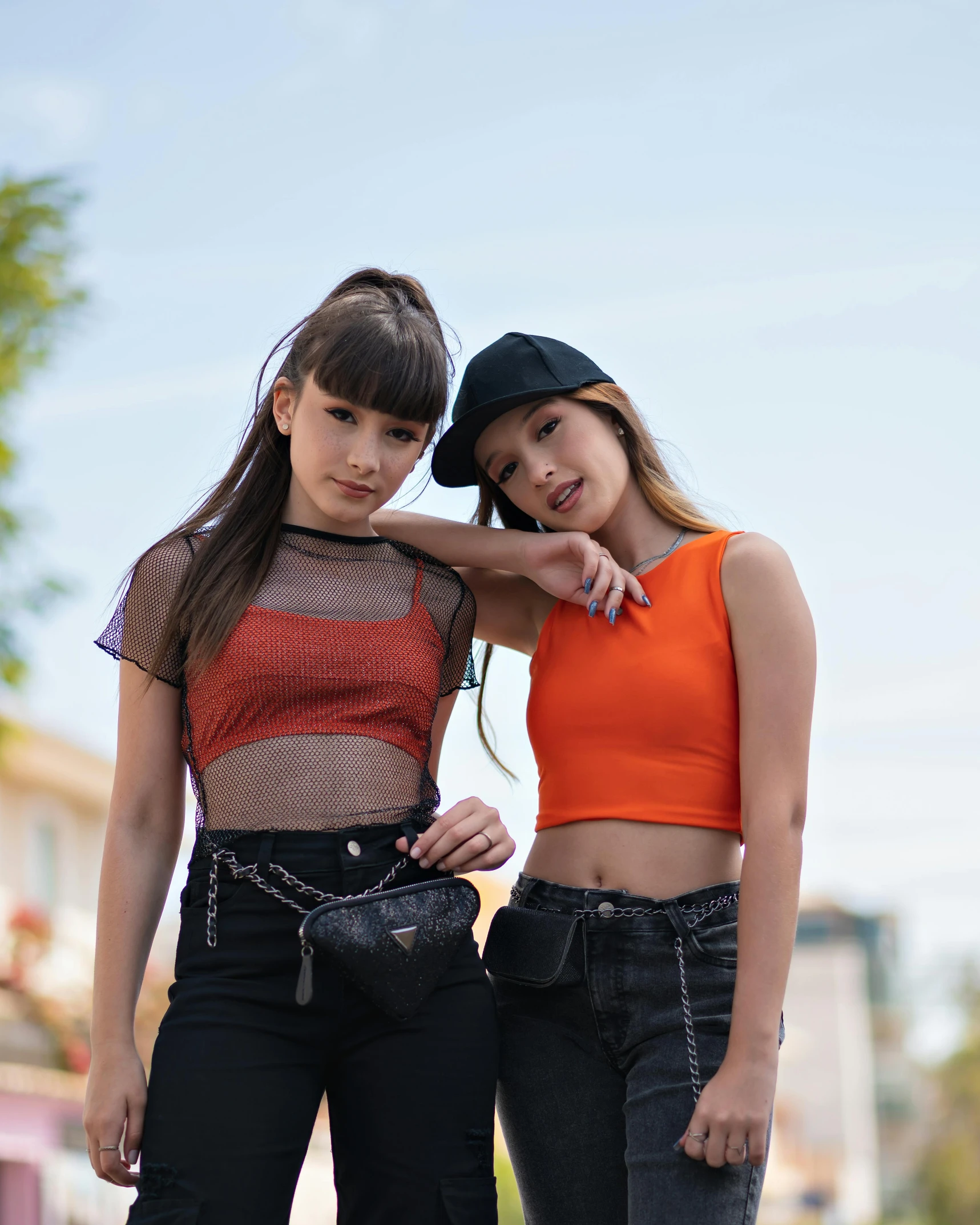 two girls in orange top and black pants stand next to each other