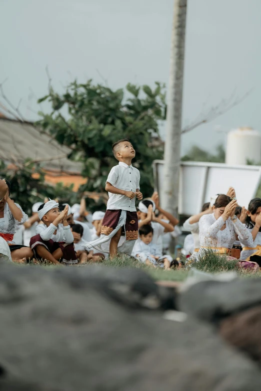 a child standing with one hand raised in front of other and a group of people behind him