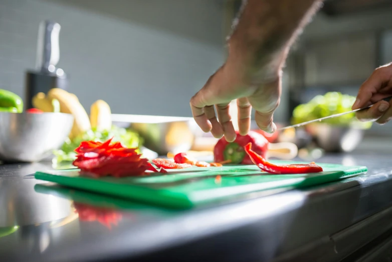 someone cuts red peppers on a green board in a kitchen