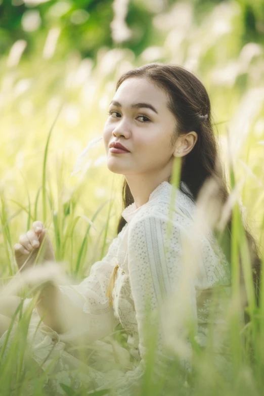 a woman sitting in the tall grass with her hair blowing