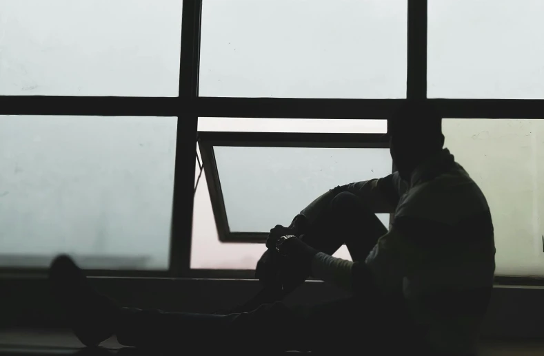 silhouette of a man sitting by a window next to a pole