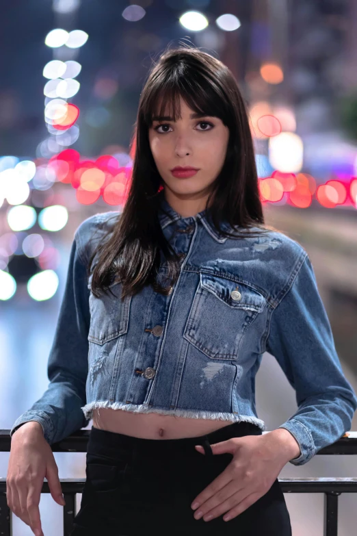 a woman wearing a jean jacket standing on the edge of a bridge