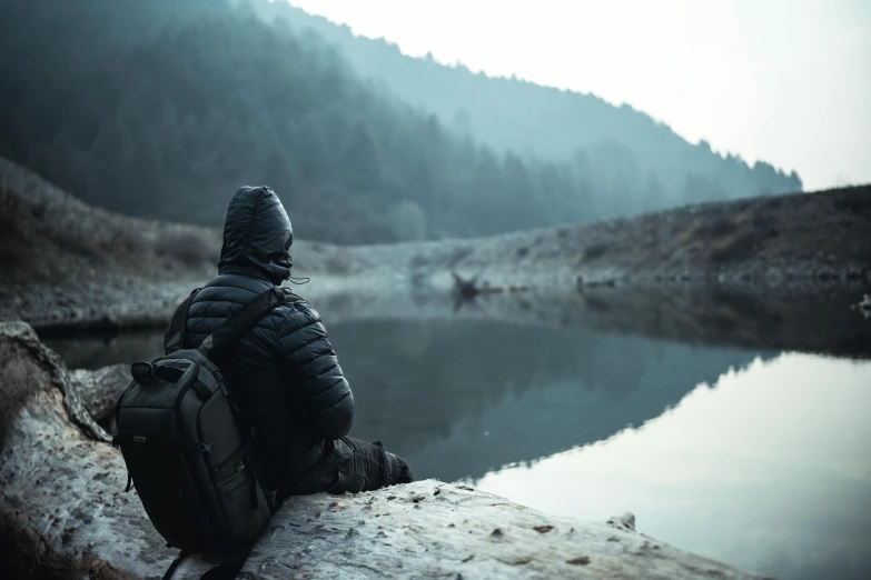 a man in a hat sits on a log beside the water