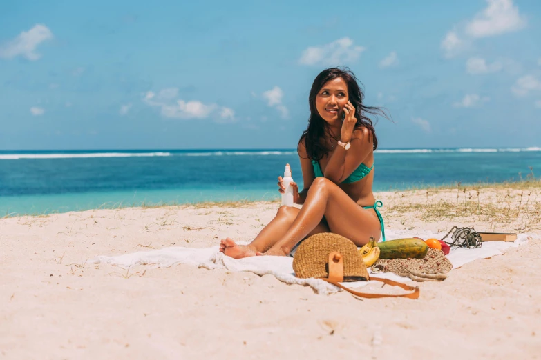 a woman sitting on a towel talking on her phone