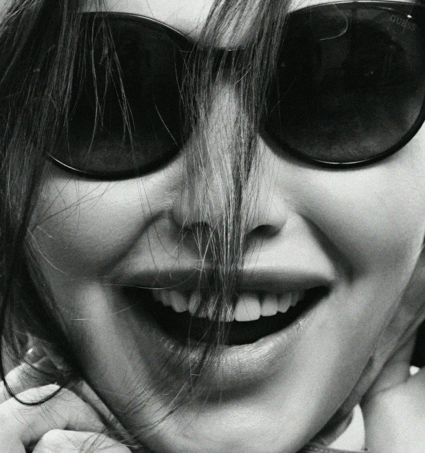 a woman wearing sunglasses and smiling while she holds her neck