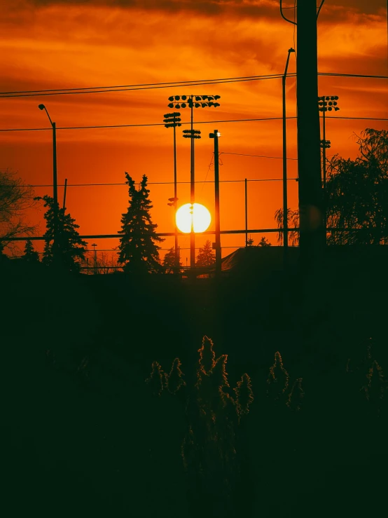 an orange sun setting behind two electric poles