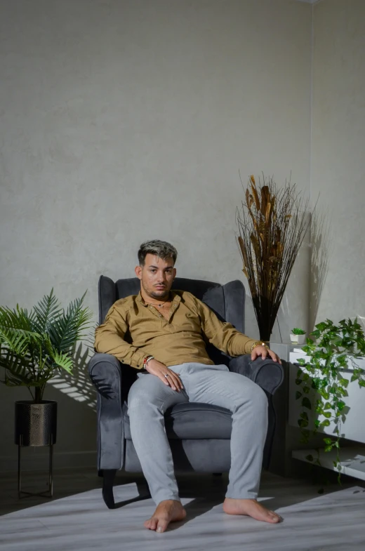 a man sits on a grey chair in front of some houseplants