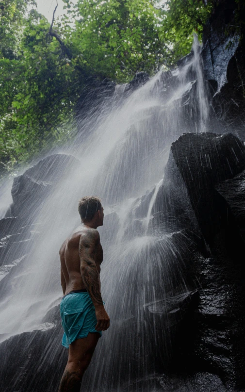 a man in trunks standing by water with trees behind him