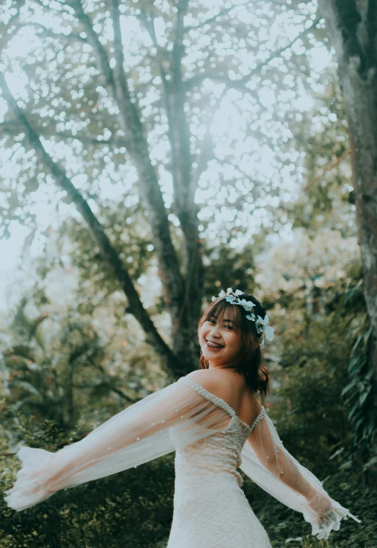 a woman wearing a wedding dress in front of a forest