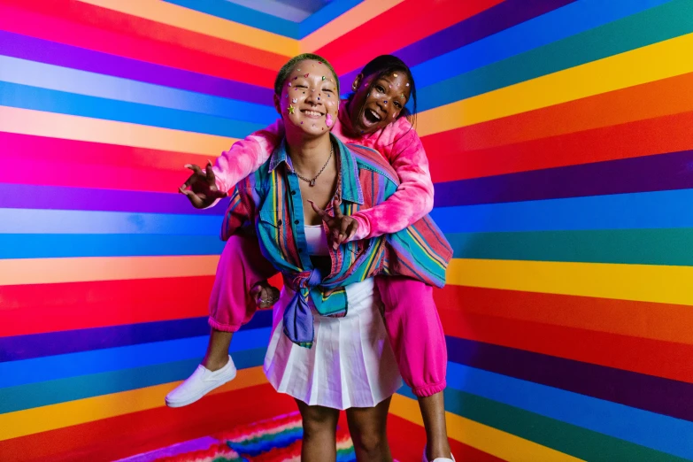two women stand against a colorful backdrop and have their arms around each other