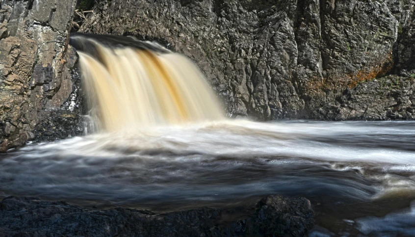 a waterfall near a rock cliff during the day