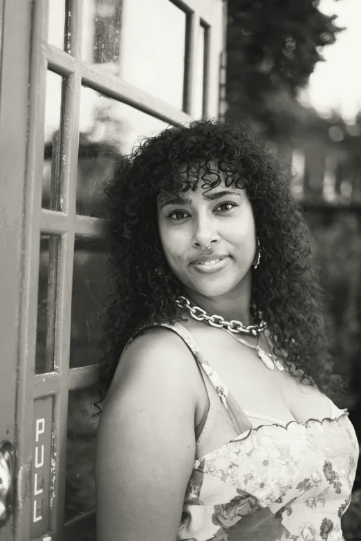 a woman with long black curly hair is posing by a telephone