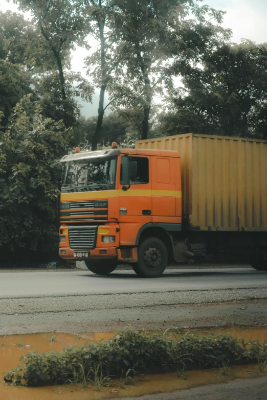 an orange delivery truck driving past lots of trees