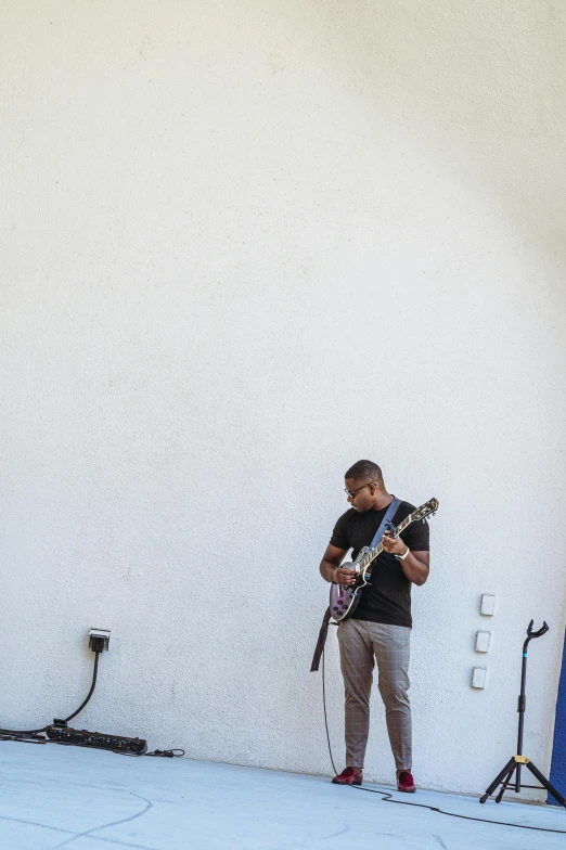 a man with a guitar is standing in front of a wall