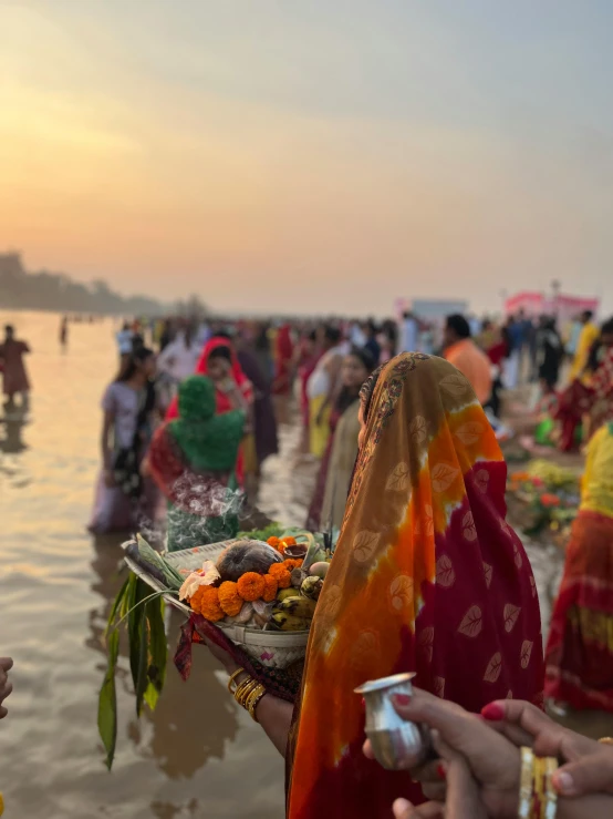 a lady in an orange scarf is eating from a tray near a lake