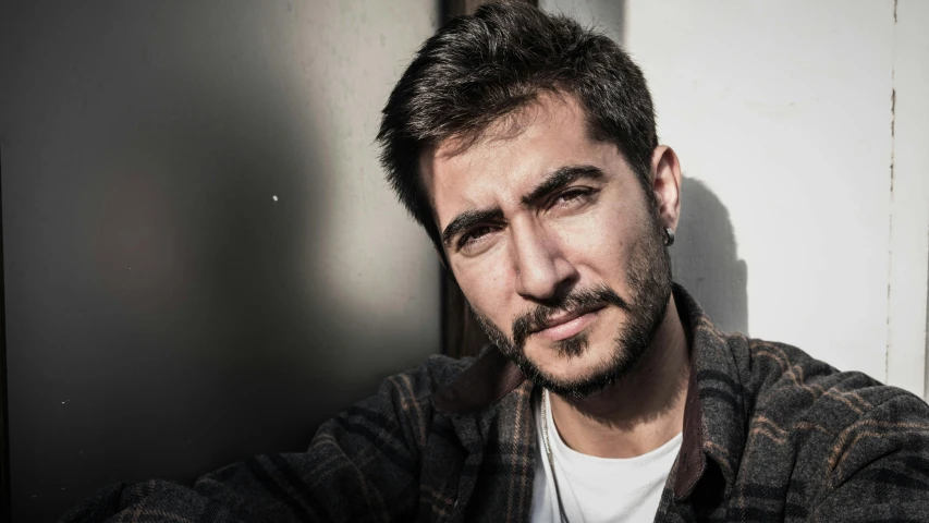 a young man leaning against a wall and looking into the camera