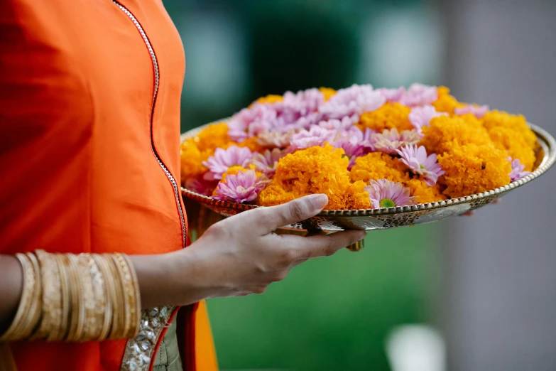a woman in an orange sari carrying a tray filled with flowers