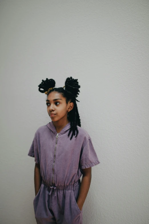 a little girl with black hair stands against a white wall