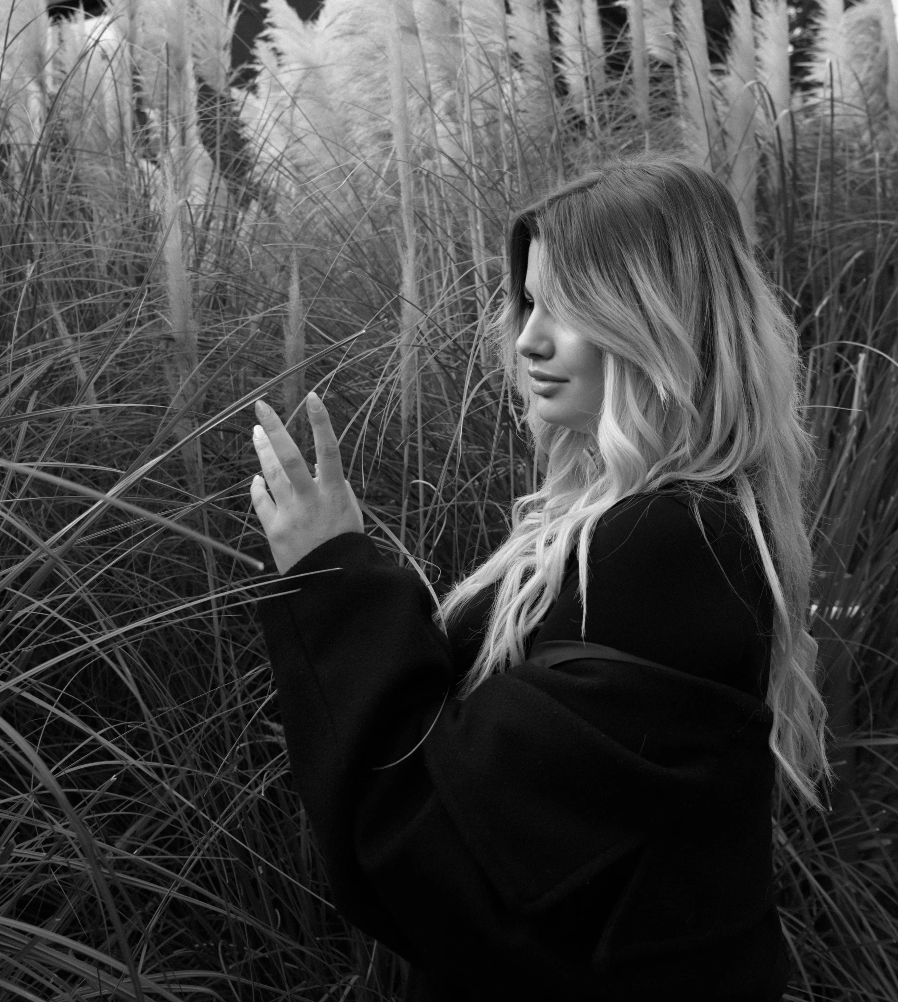 a girl standing among tall grass and other plants looking at her phone