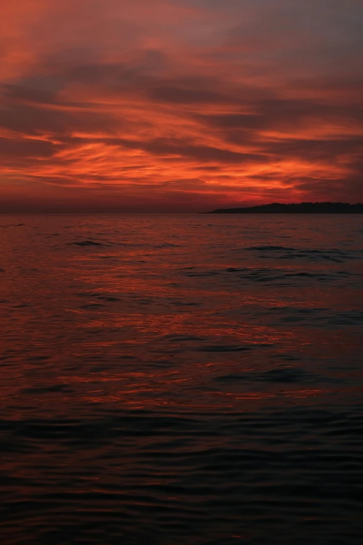 a bright red sky with some clouds and water