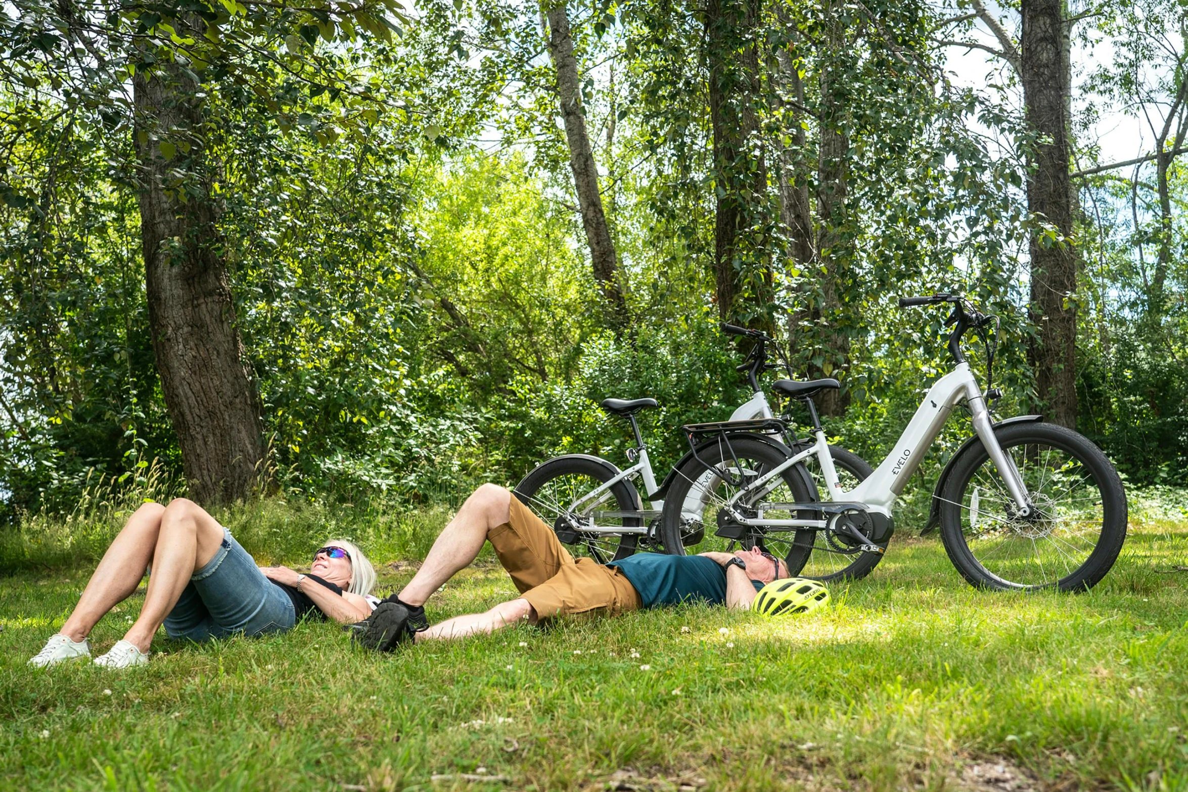 two people laying on the grass with a bike in the background