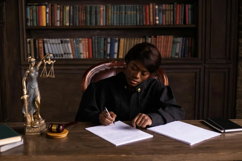 a woman sitting at a table doing paperwork with a judge statue in the background