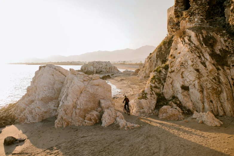 a man standing on the shore in front of a big rock