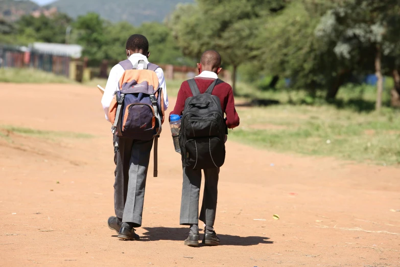 two young men with back packs walking down a dirt road