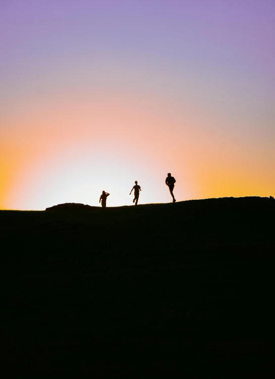 three people are standing on the top of a hill at sunrise