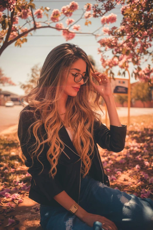 a woman wearing glasses sitting in the shade by some blossom