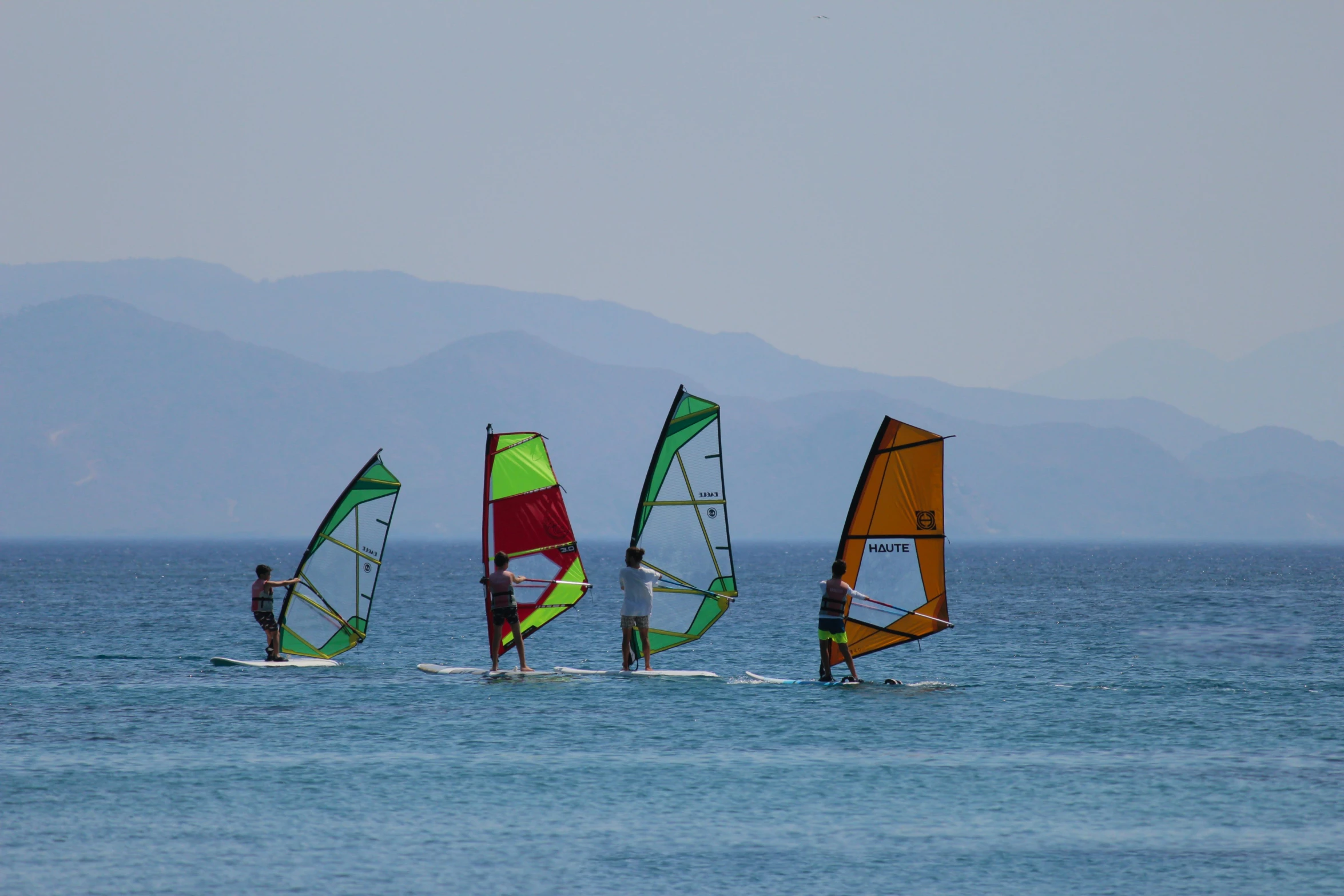 three small sailboats are in the water, one is on a surfboard