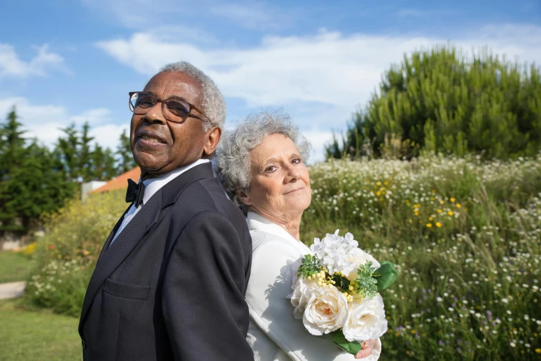 a man and woman posing in front of trees and flowers