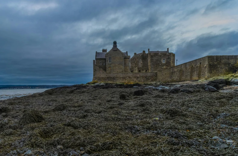 an old castle sitting on the shore with grey clouds