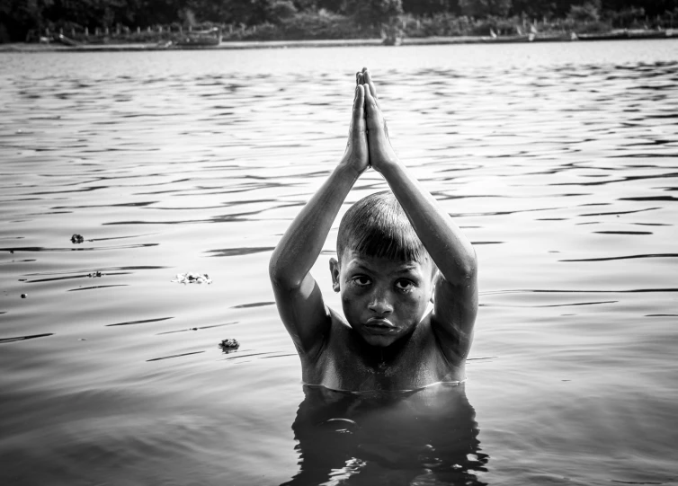 a boy is sitting in the water making a peace sign