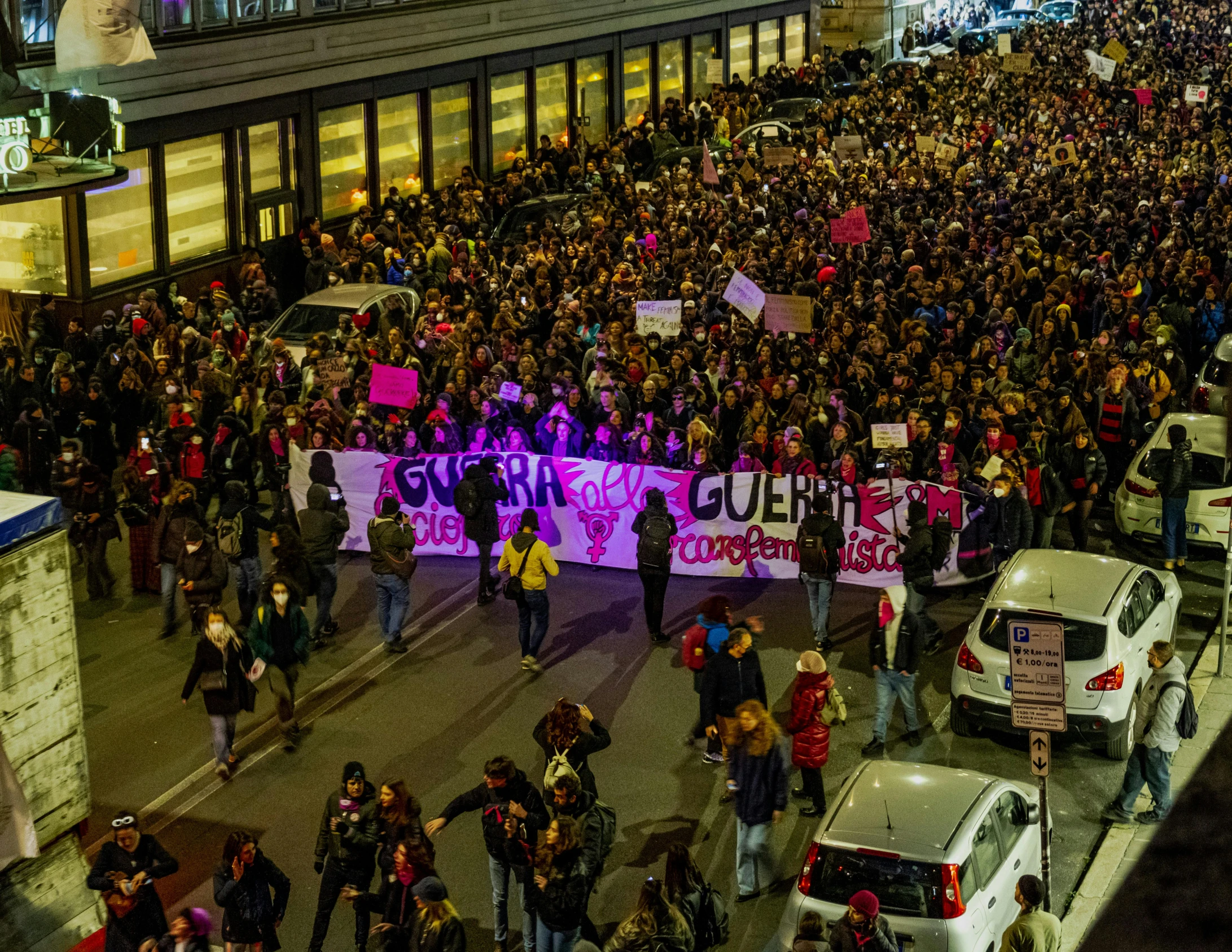 a large group of protesters march through a street in front of buildings at night