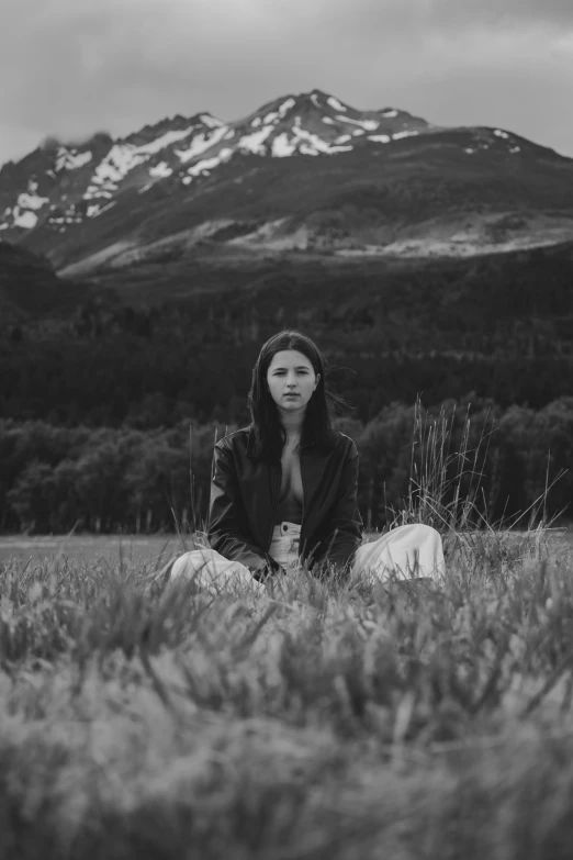 a woman is sitting in a field in front of a mountain