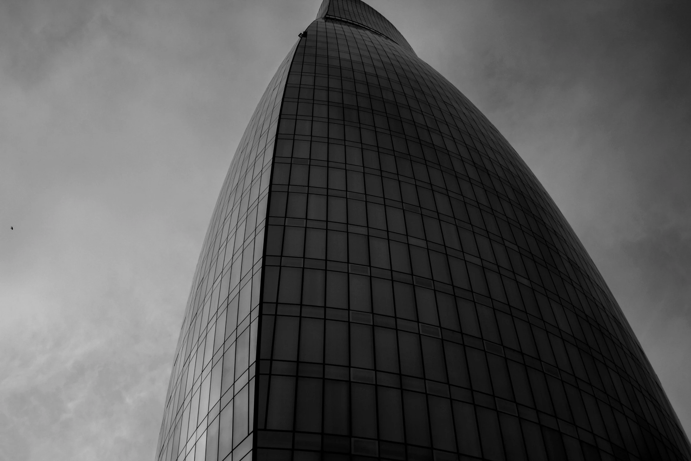 a tall glass building with a cloudy sky in the background