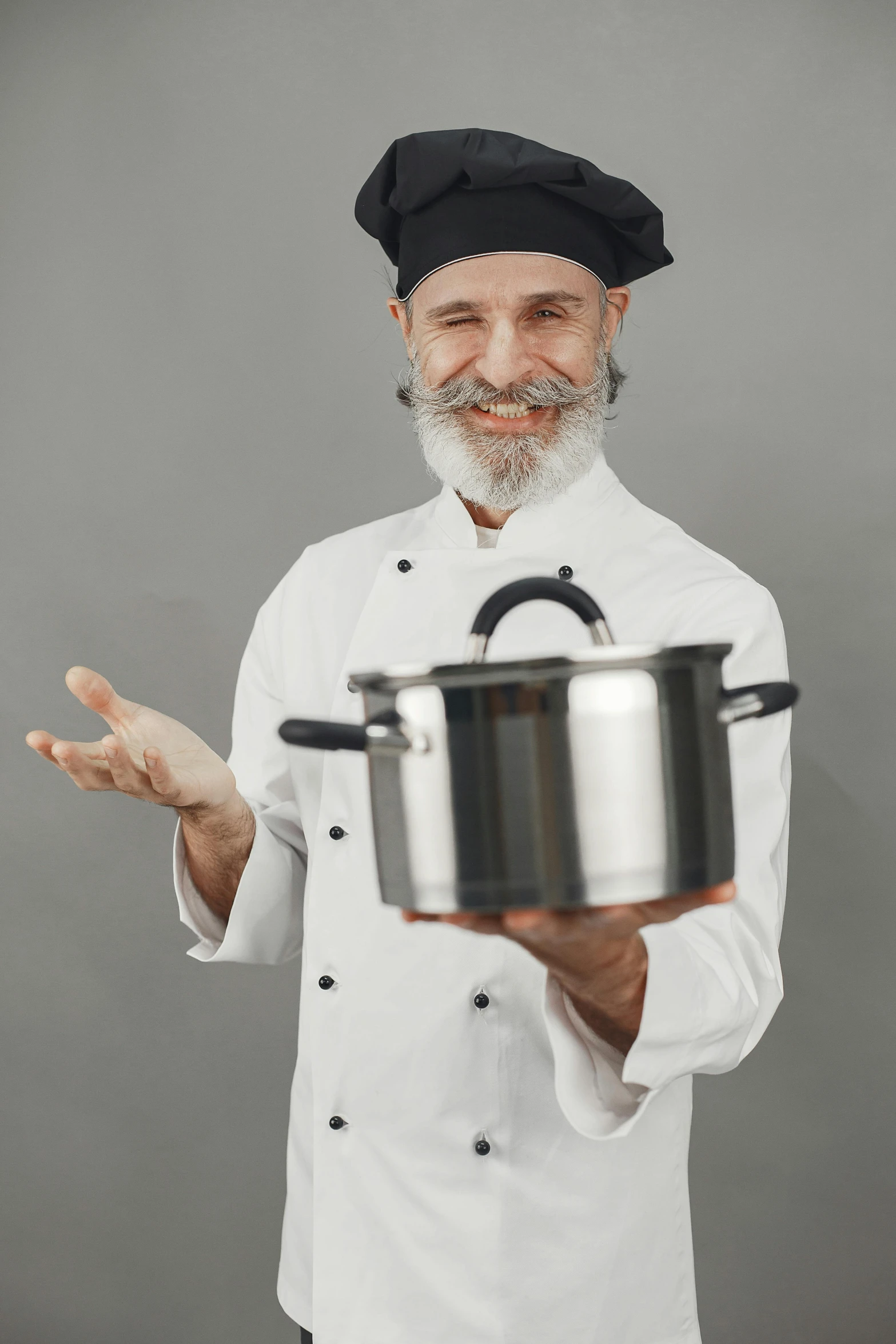 a smiling chef wearing a white uniform and holding a pan