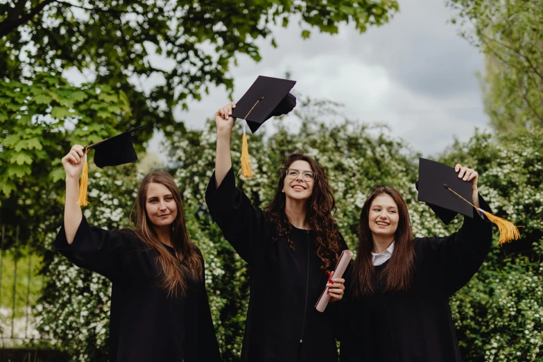 three beautiful young women holding up their graduation caps