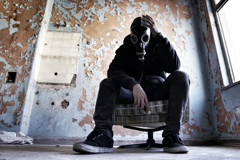 a man in black hood and a mask sitting on a chair
