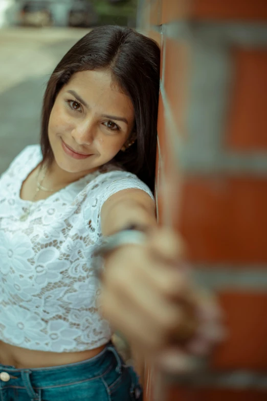 a smiling woman leans against the wall next to a brick building