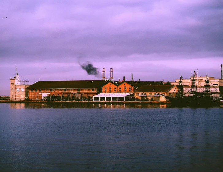 an old factory sits on the waters edge with smoke coming out of stacks