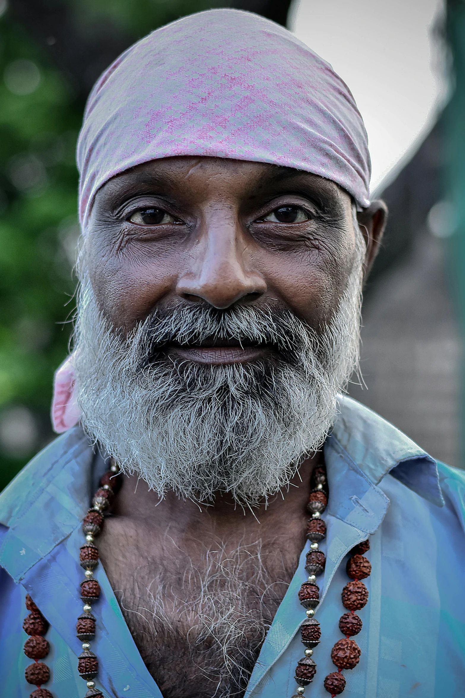 an old man wearing a pink hat and beaded necklace