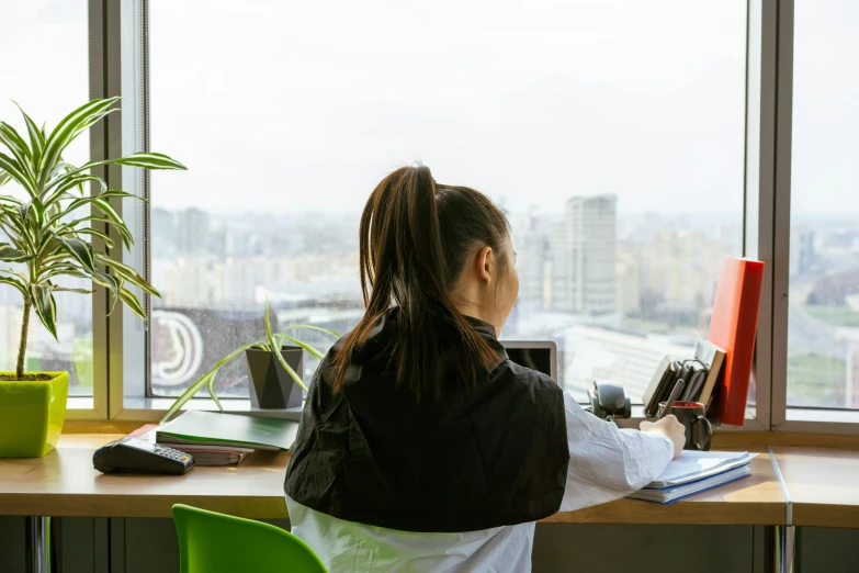 a woman sitting at a desk looking out a large window