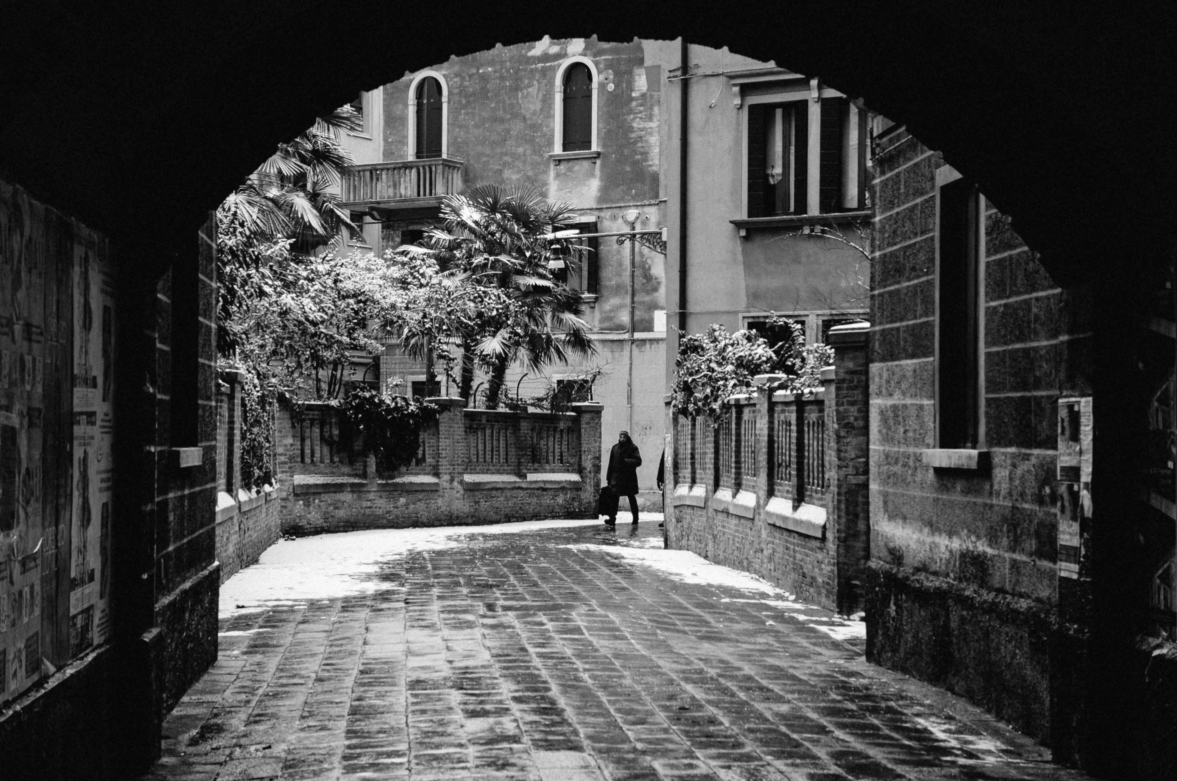 a person walking down a sidewalk under a arched doorway